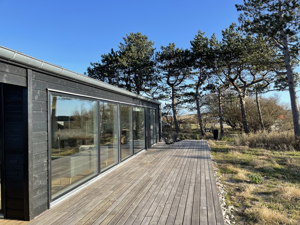 Modernes dunkles Ferienhaus mit großer Holzterrasse unter blauem Himmel